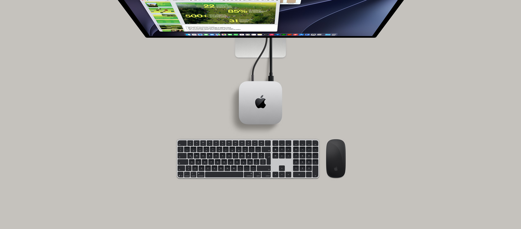 Mac mini, parte superior, aluminio color plata, esquinas redondeadas, logo de Apple en el centro en color negro brillante, conectada con un cable, monitor Studio Display parcialmente visible en la parte superior con la app Calendario, una presentación de Keynote y una gráfica de barras, Magic Keyboard con teclado numérico, Magic Mouse debajo del Mac mini