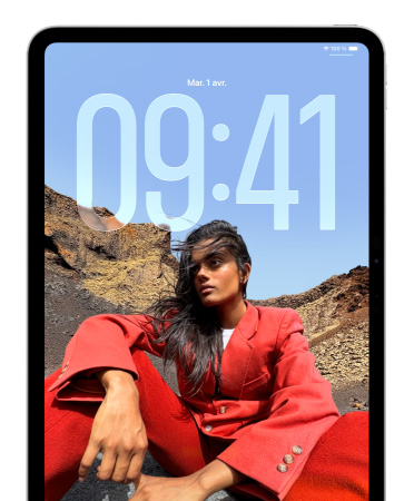 Un iPad affiche l’écran verrouillé où les chiffres de l’heure apparaissent derrière la photo d’une personne assise
