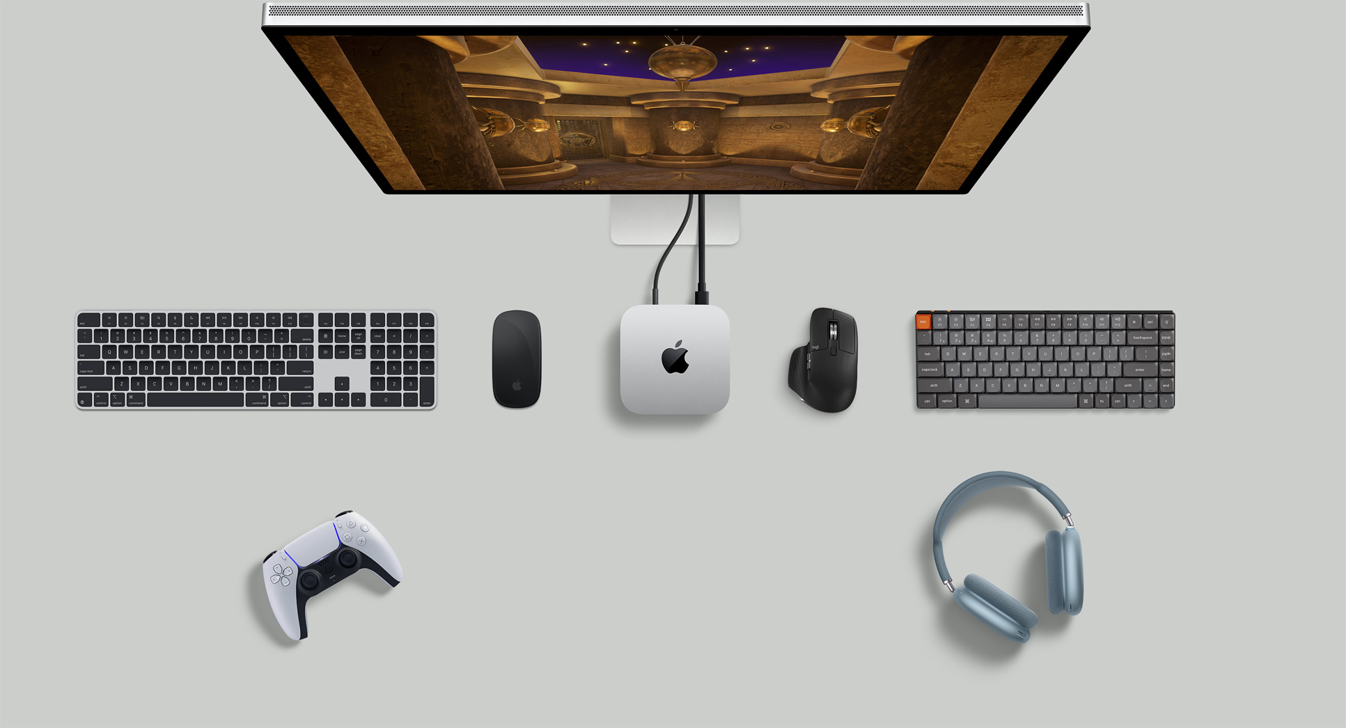 Widok z góry przedstawiający srebrnego Maca mini, urządzenie jest ustawione do pracy przy biurku i pokazane z ekranem wyświetlacza, bezprzewodową klawiaturą, bezprzewodową myszą, kontrolerem do gier i słuchawkami AirPods Max