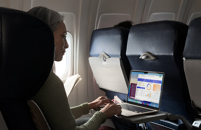 Uçakta koltukta oturan bir kişi MacBook Air’inde çalışıyor
